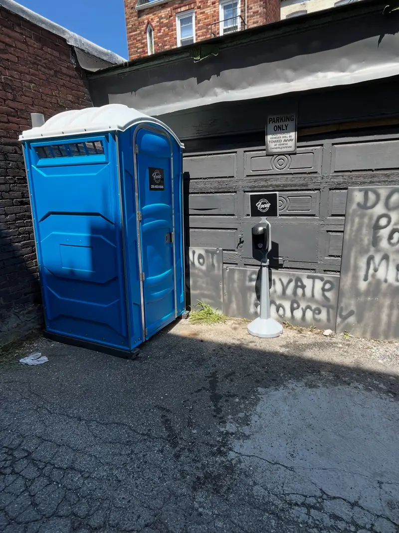 Blue portable toilet placed beside a garage on a residential driveway