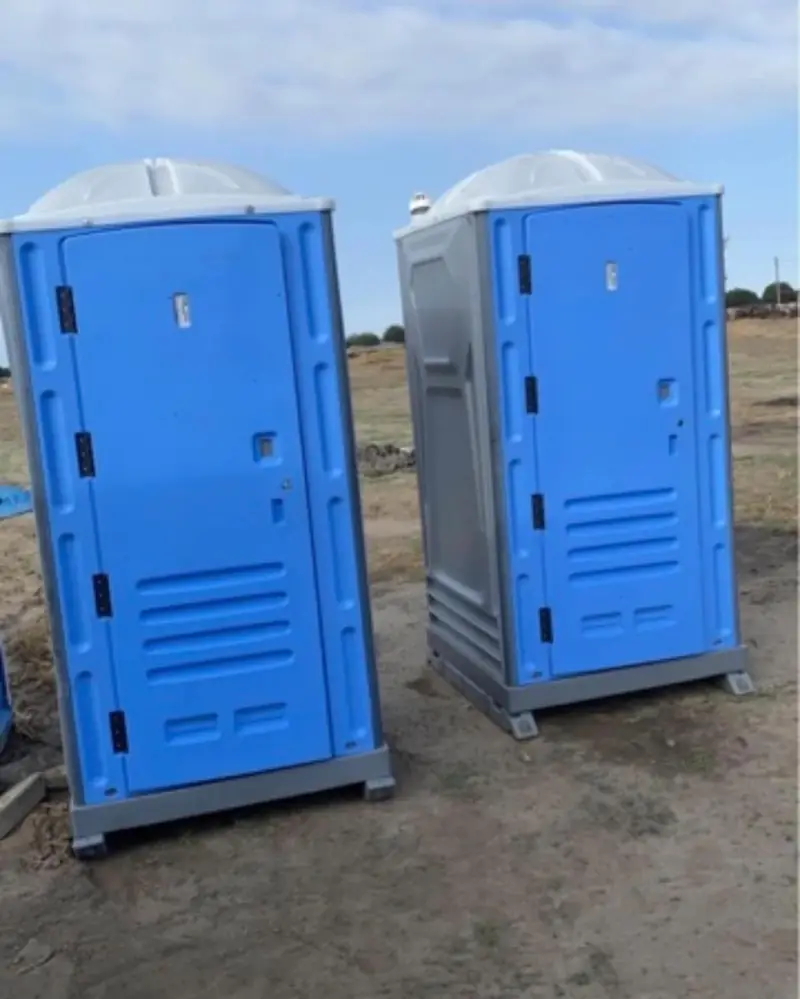 Two standard blue portable toilets set on a dirt job site
